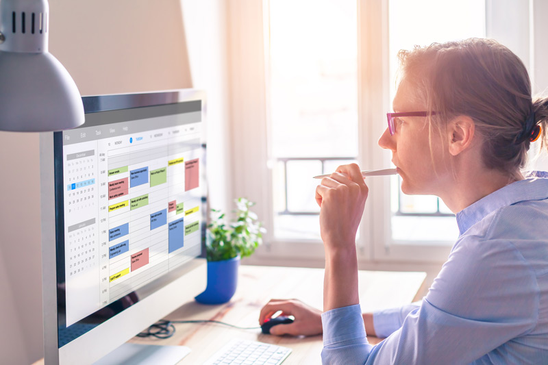 Frau im Buero vor einem Computer-Bildschirm mit einem Stift in der Hand, schaut sich einen digitalen Kalender an