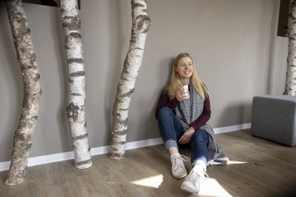 Auszubildende Tourismuskauffrau Karina auf dem Boden sitzend mit einer Kaffeetasse in der Hand
