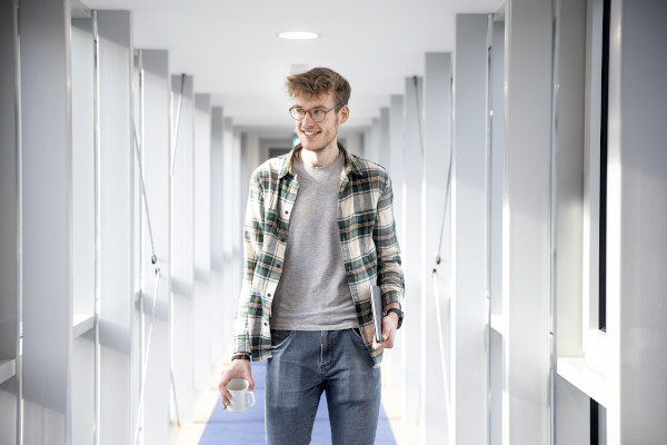 Auszubildender im E-Commerce Felix im Flur mit einer Kaffeetasse in der Hand